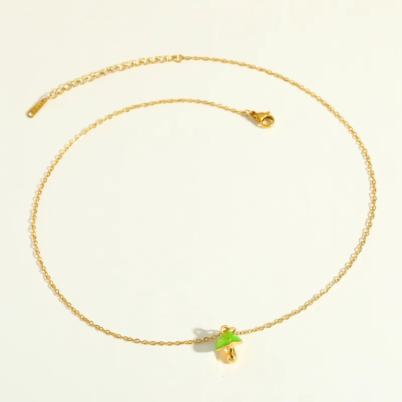 Gold anklet with a green acorn charm on a light beige background