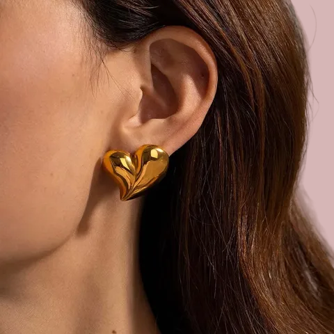 Gold heart-shaped earring worn by a person with brown hair.