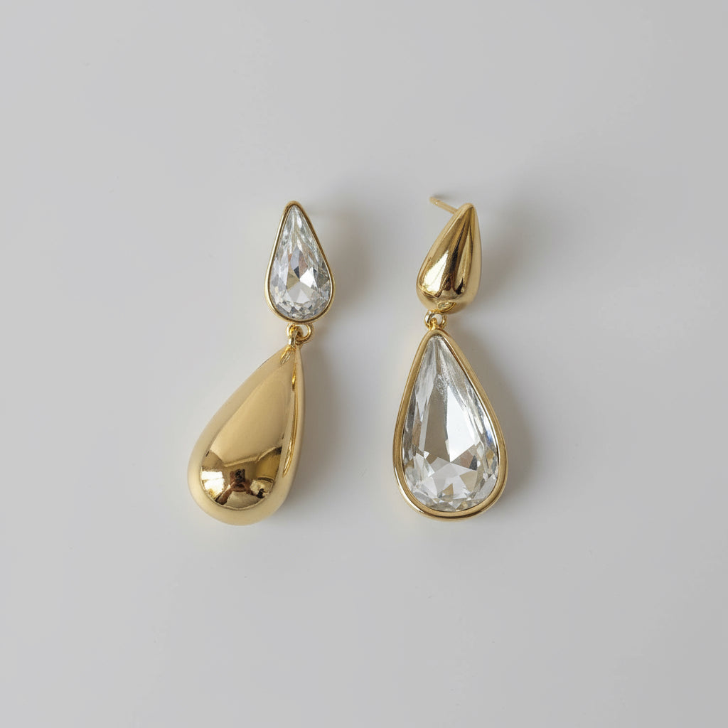 Gold teardrop-shaped earrings on a light gray fabric background