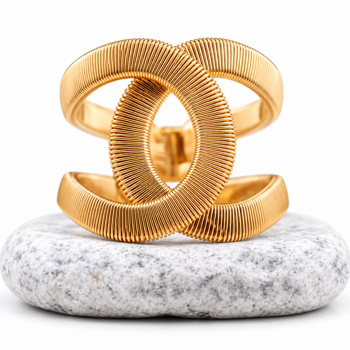 A gold-toned open cuff bracelet with a ribbed, textured design, displayed on a smooth white and gray stone against a clean white background.