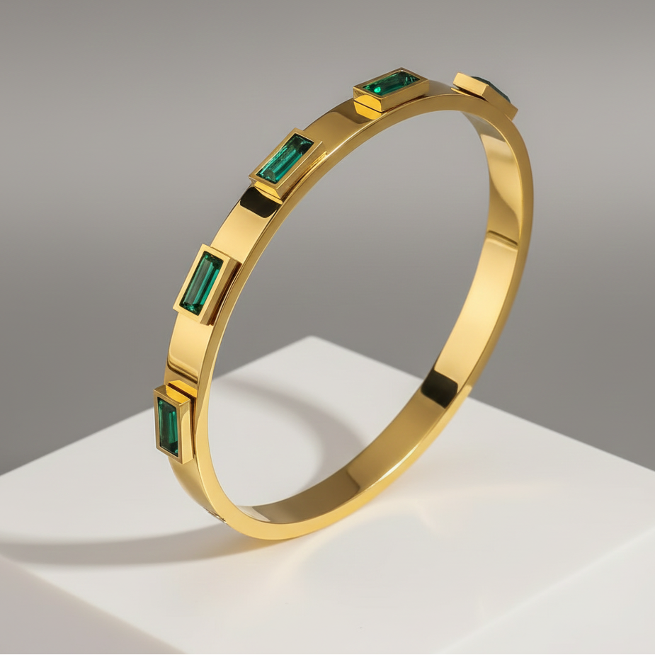 Gold bracelet with emerald green stones on a gray background