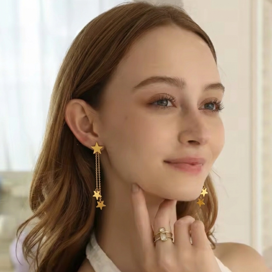 Woman wearing gold star earrings and a ring, with a blurred indoor background