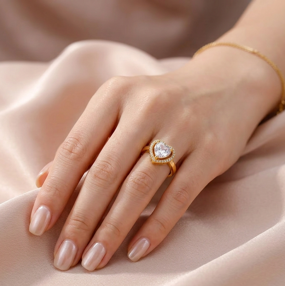 Hand wearing a gold ring with a heart-shaped gemstone on a soft fabric background