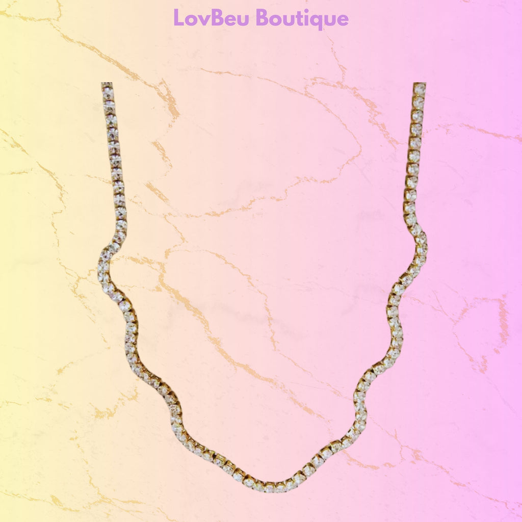 A wavy, scalloped necklace paved with clear rhinestones, displayed on a pastel pink and yellow marble-textured background with the text 'LovBeu Boutique' at the top.