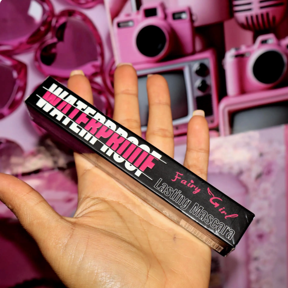Hand holding a mascara tube labeled 'Waterproof' with pink camera-themed background