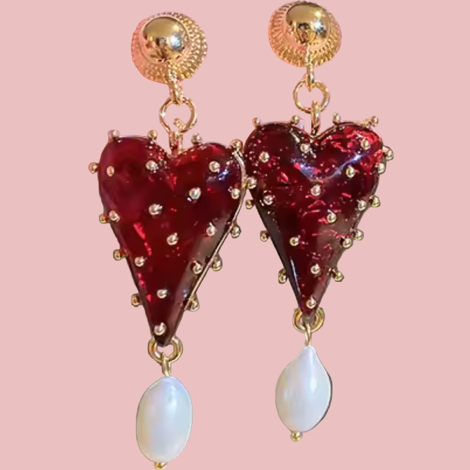 Heart-shaped earrings with gold accents held by a hand against a neutral background
