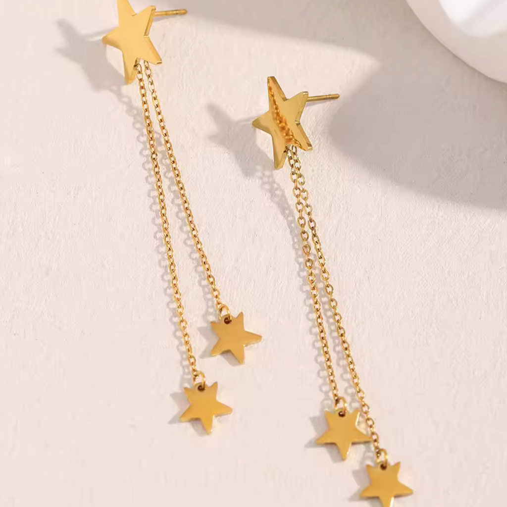 Gold star earrings with chain on a light background