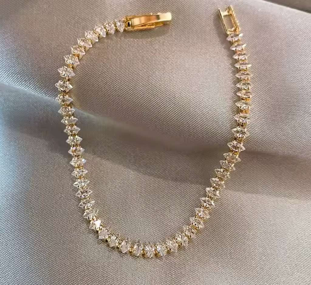 Gold bracelet with clear stones on a gray fabric background