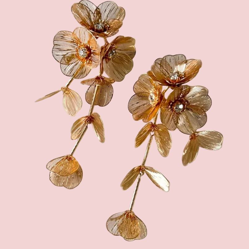 Gold floral earrings on a white textured surface