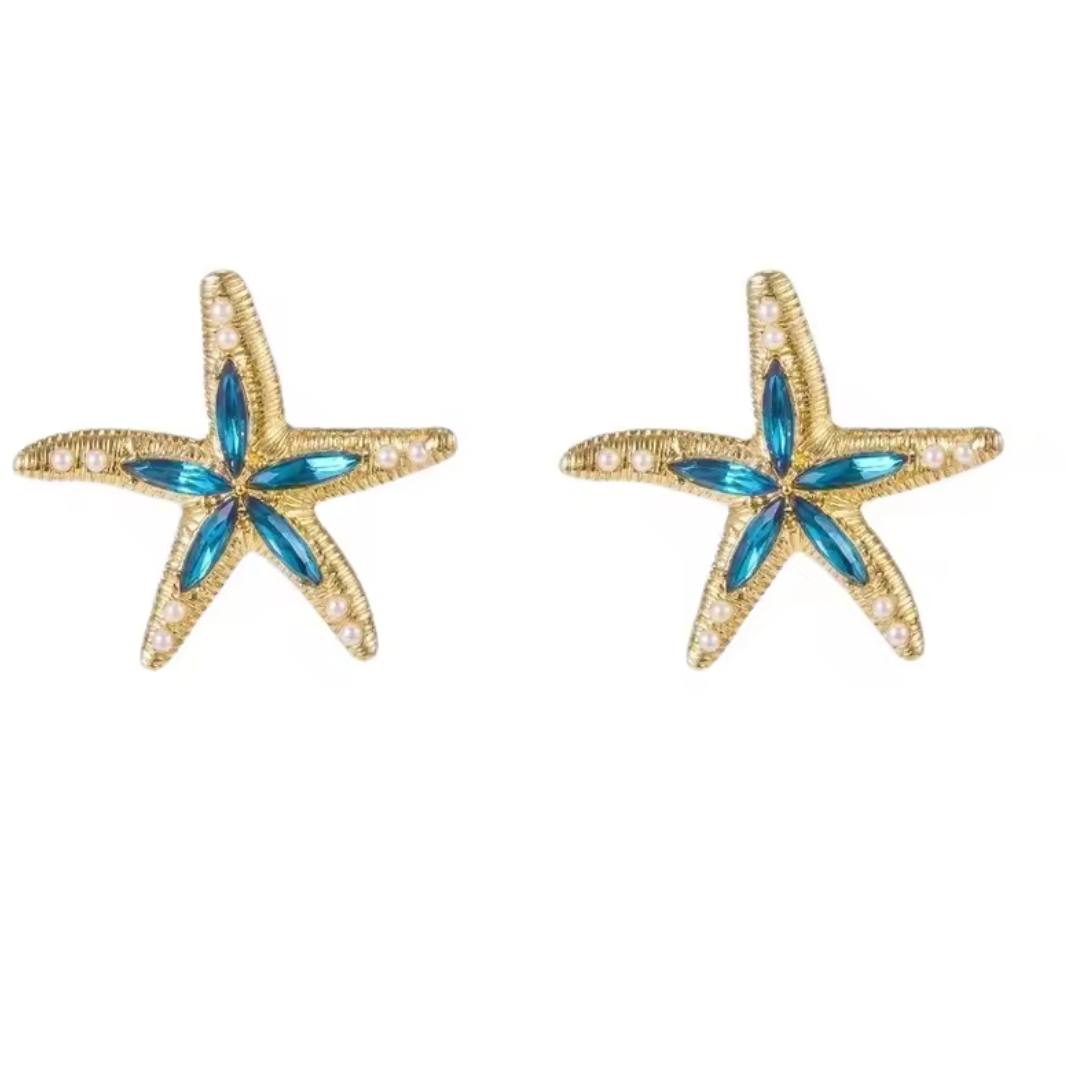 A pair of gold starfish stud earrings with blue marquise-cut center stones and small clear rhinestone accents along the arms, shown on a plain white background.