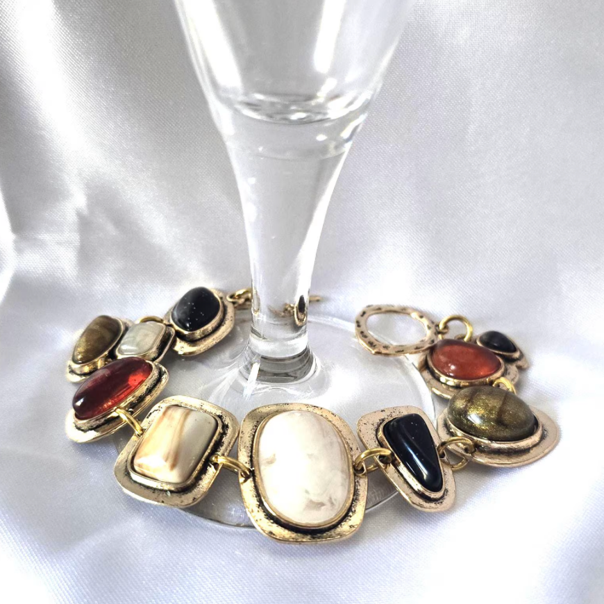 Bracelet with multicolored stones on a white surface next to a clear glass.