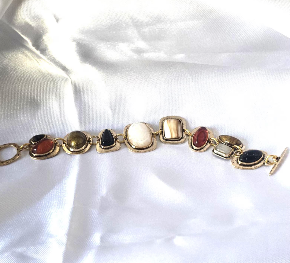 Gold bracelet with multicolored stones on a white satin background