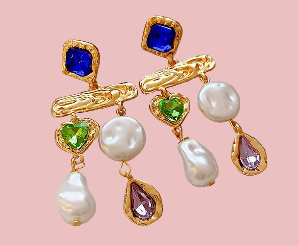 Gold earrings with pearls and colored gemstones on a beige fabric background