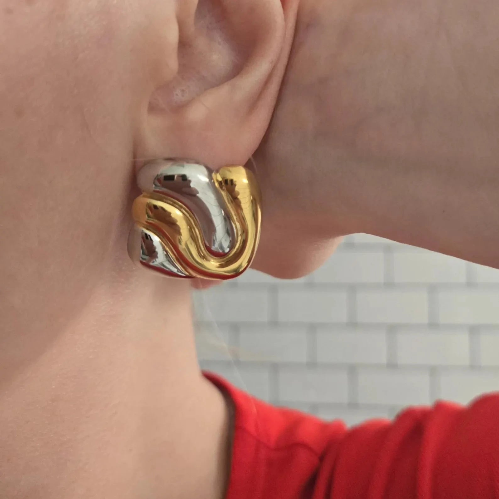 Close-up of a person wearing a gold and silver spiral earring with a blurred background.